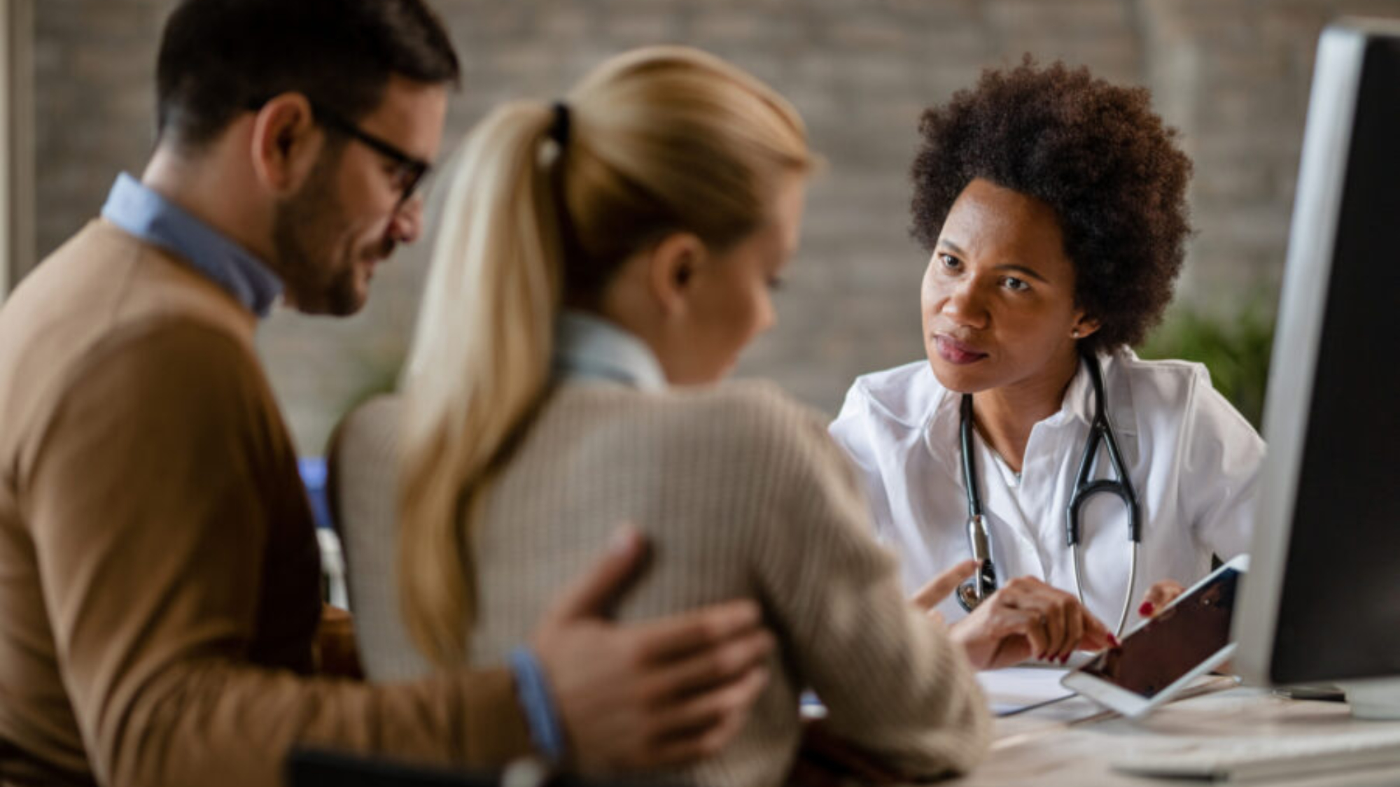 Black female doctor showing to a couple their electronic medical record on touchpad while communicating with them at clinic.
