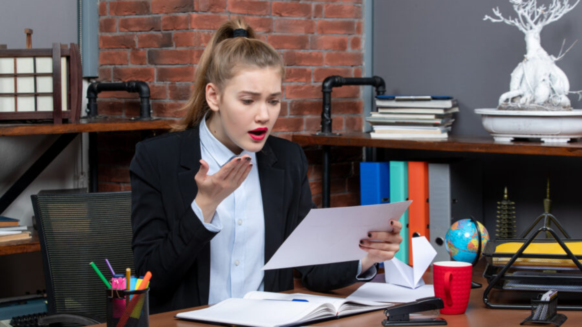 top-view-young-woman-sitting-table-holding-document-reading-something-with-confused-facial-expression-office