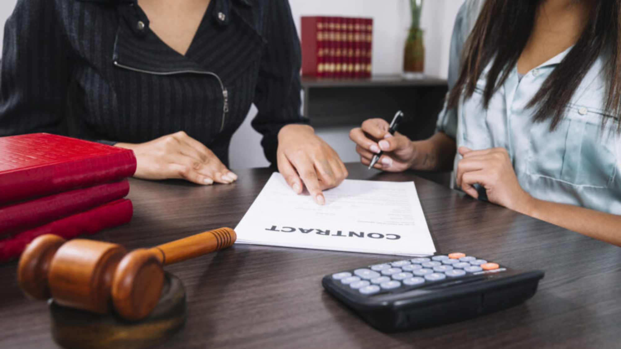 black-woman-pointing-document-near-lady-with-pen-table-with-calculator-gavel
